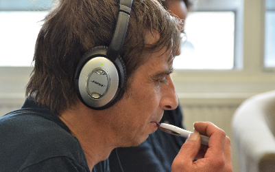 White man with dark hair wearing headphones and holding a pen.