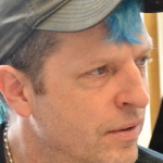 White man wearing a baseball cap with blue hair.