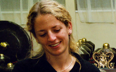 A white, blonde woman smiling and looking down while playing gamelan.