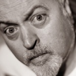 Close up on Bill Bailey, a white middled aged man with long grey hair and a beard.